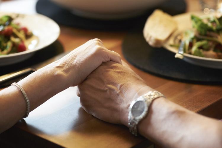 Closeup cropped image of a couple holding hands across a table filled with food